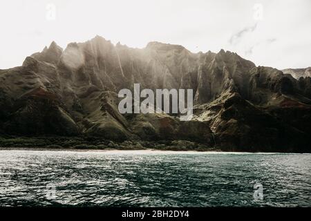 Beautiful mountain range and sea against sky at Nā Pali Coast State Wilderness Park, Kauai, Hawaii, USA Stock Photo