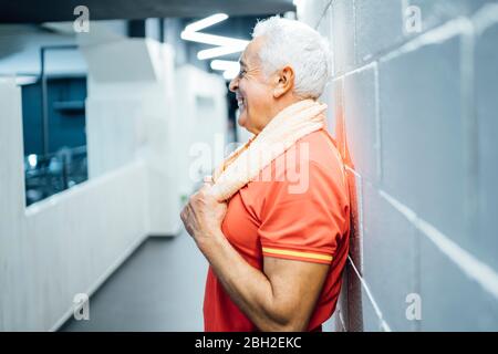 Happy senior man having a break and leaning agianst a wall in gym Stock Photo