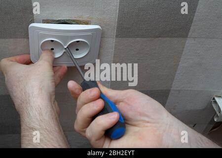 Repair of an electrical outlet in a city apartment. Visible insulated wires, disassembled power outlet. A hole has been made in the wall Stock Photo