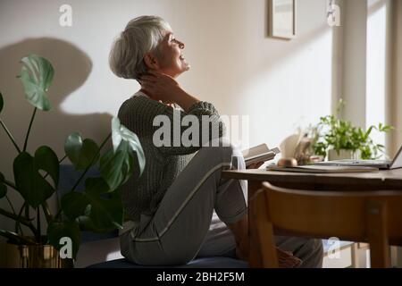 Confident senior woman with notebook and laptop relaxing at home Stock Photo