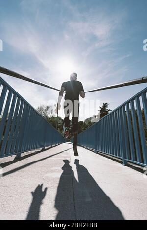 Rear view of disabled athlete with leg prosthesis running on a bridge Stock Photo