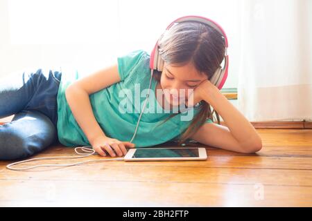 Girl lying on the floor at home using headphones and digital tablet Stock Photo