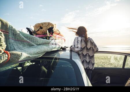 Back view of woman with car on the beach looking to the sea, Tafedna, Morocco Stock Photo