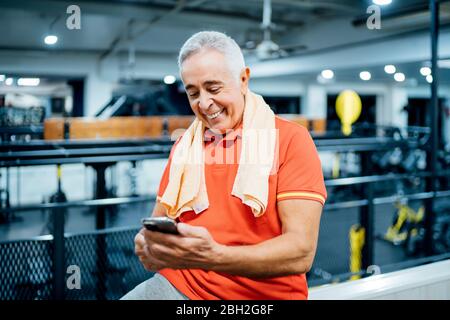 Happy senior man having a break and using cell phone in gym Stock Photo