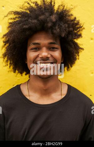 Portrait of happy young man with afro against yellow wall Stock Photo