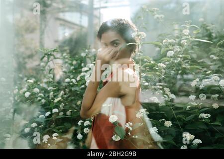 Portrait of young woman standing behind glass pane in an urban garden Stock Photo