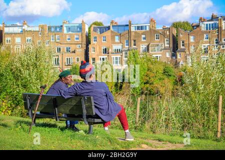 London, UK - October 5, 2019 - Two men sitting on a bench looking over the neighbouring estates at Hampstead Heath Stock Photo