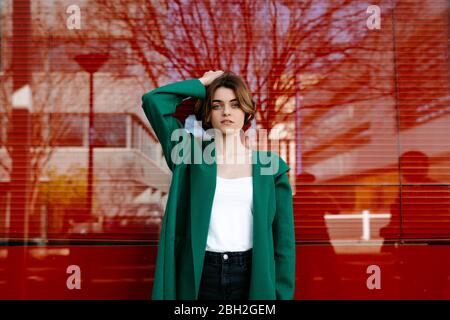 Young woman wearing green coat in front of a glass pane Stock Photo