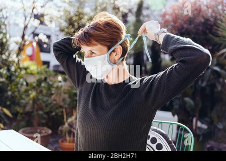 Woman siting in garden, putting on face mask Stock Photo