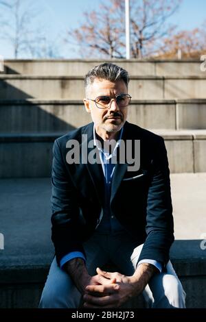 Gray-haired businessman sitting on stairs outdoors Stock Photo