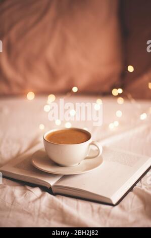 Fresh cup of coffee on paper book indoors in bed closeup. Good morning. Stock Photo