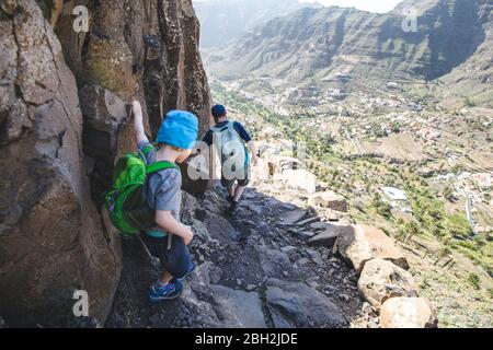 Back view of father and little son with backpacks on a hiking trail in the mountains, La Gomera, Canary Islands, Spain Stock Photo