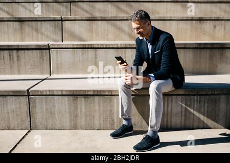 Gray-haired businessman sitting on stairs using cell phone Stock Photo