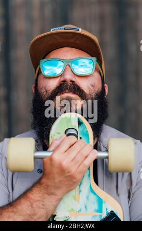 Portrait of bearded man with skateboard wearing mirrored sunglasses Stock Photo