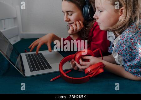 Two sisters with headphones lying on bed using laptop Stock Photo