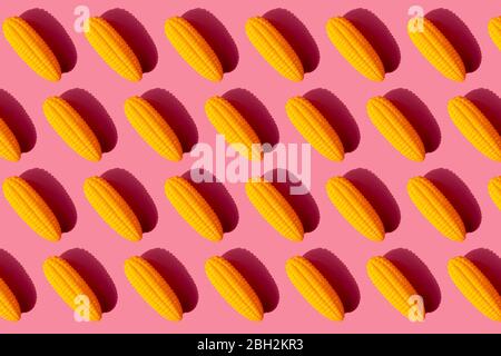 Pattern of yellow plastic corn cobs against pink background Stock Photo