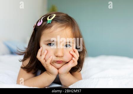 Portrait of bored little girl lying on bed Stock Photo