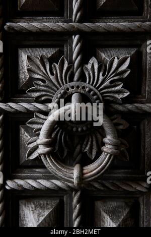 Detailed close-up of large ancient hand carved wooden door and round knocker Stock Photo