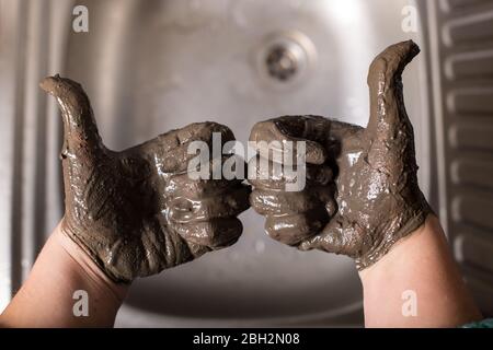 Hands in mud showing a thumbs with sink on background. Stock Photo