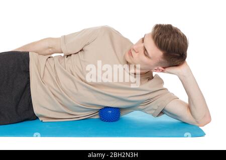 Handsome man shows exercises using the ball with spikes for a myofascial release massage of trigger points. Massage of the broadest back muscle. Isola Stock Photo