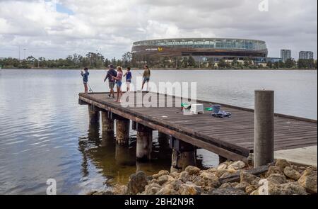 Father and children fishing off a wooden jetty on the Swan River and Optus Stadium Perth Western Australia. Stock Photo