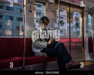 A man wearing a mask looks at his smartphone inside a suburb train for Shinjuku in Tokyo, Japan, 23 April 2020. Japanese Prime Minister Shinzo Abe extends state of emergency for Japan area for at least until second week of May on increase of coronavirus and COVID-19 infection cases. April 23, 2020 Credit: Nicolas Datiche/AFLO/Alamy Live News Stock Photo