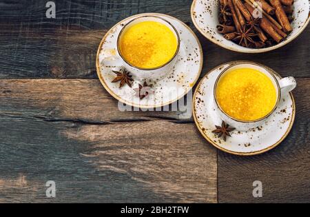 Hot turmeric curcuma milk drink with spices on dark wooden background Stock Photo