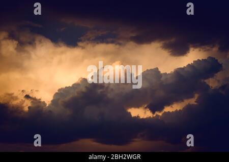 Dark, dramatic nimbus clouds at sunset, lit by the last rays of sunlight before a storm. Stock Photo