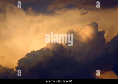 Dark, dramatic nimbus clouds at sunset, lit by the last rays of sunlight before a storm. Stock Photo