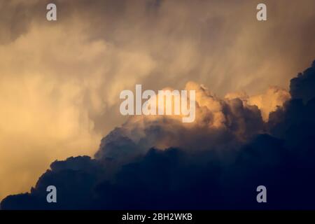 Dark, dramatic nimbus clouds at sunset, lit by the last rays of sunlight before a storm. Stock Photo