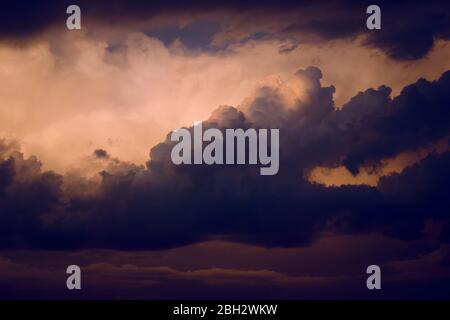 Dark, dramatic nimbus clouds at sunset, lit by the last rays of sunlight before a storm. Stock Photo