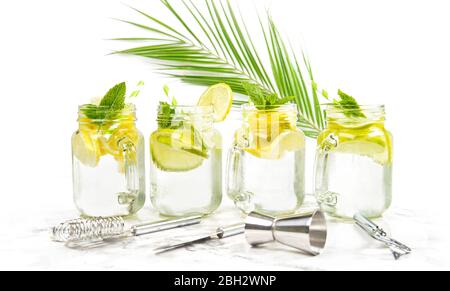 Cocktail drink with lime, lemon, mint and ice. Bar tools and palm leaves decoration on white background Stock Photo