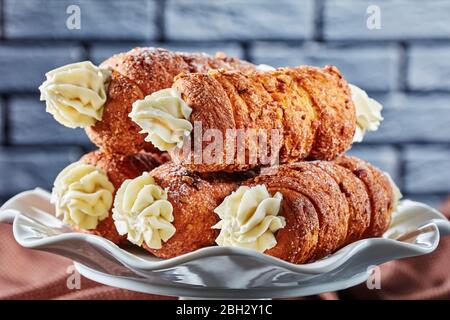 Dessert tubes filled with cream served on a white cake stand in front of a black brick wall on a dark concrete background, close-up Stock Photo