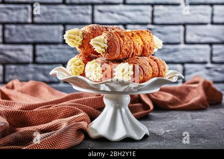 Czech kremrole: traditional pastry filled with buttercream frosting, served on a white cake stand in front of black brick wall on a dark concrete back Stock Photo