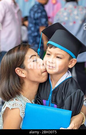 Portrait son graduated from kindergarten and mother kissing . Stock Photo