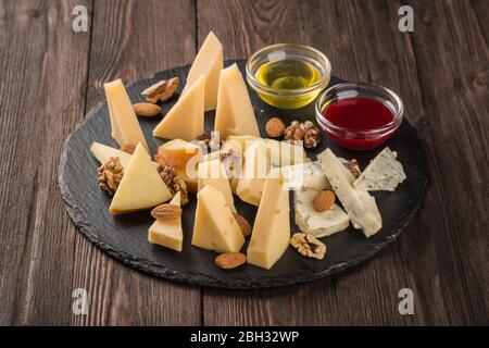Assorted cheeses on a black dish. Served with nuts sauce and honey. Stock Photo