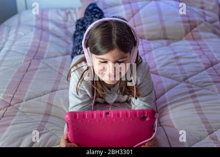 Cute little girl using tablet while lying in bed Stock Photo