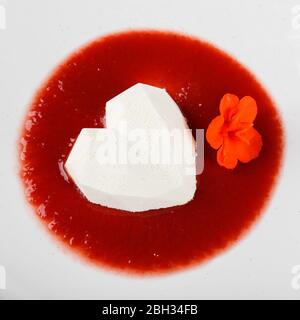 White heart-shaped mousse dessert with red fruit sauce in a plate. Stock Photo