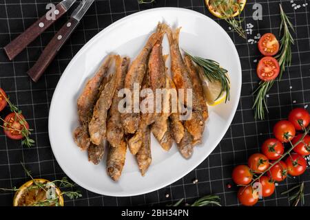 A dish of fried red mullet. Table setting, decorated with greens and cherry tomatoes. Stock Photo