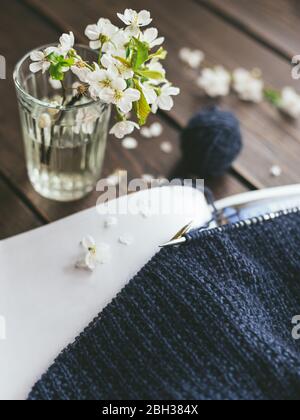 Hand knitting with needle, yarn ball and glass with spring blossom on a dark wooden background. Concept for handmade and hygge slow life. Stock Photo
