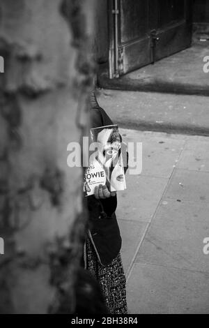 photo of David Bowie as Ziggy Stardust, cover of The Big Issue, peeking out from behind tree trunk, Stock Photo