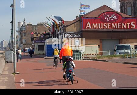 Portobello, Edinburgh, Scotland, UK. 23rd April 2020. Sunny but breezy afternoon. More local people venturing out to the seaside perhaps encouraged by the sunshine to carry out their permitted daily excercise, still almost as many cyclists as pedestrians on the Promenade. Thank You NHS flags flying proudly above the amusement arcade with the stiff breeze. Credit: Arch White/Alamy Live News. Stock Photo