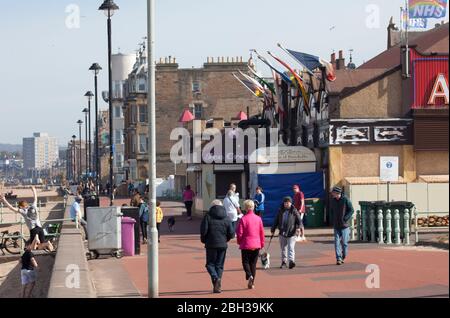 Portobello, Edinburgh, Scotland, UK. 23rd April 2020. Sunny but breezy afternoon. More local people venturing out to the seaside perhaps encouraged by the sunshine to carry out their permitted daily excercise, still almost as many cyclists as pedestrians on the Promenade. Thank You NHS flags flying proudly above the amusement arcade with the stiff breeze. Credit: Arch White/Alamy Live News. Stock Photo