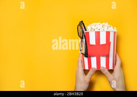 The guy holds popcorn in his hands on a yellow background. Place for text. Stock Photo