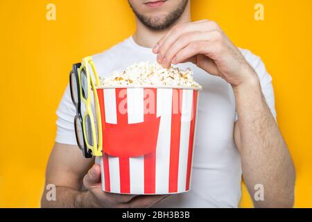 Handsome guy holds popcorn and 3D glasses. Yellow background. Close-up Stock Photo