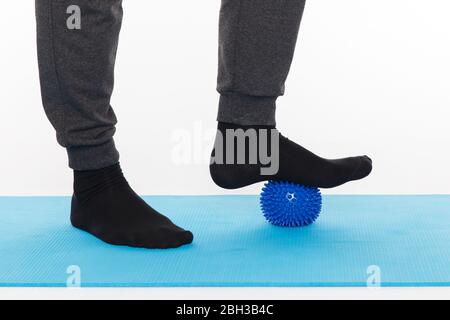 Handsome man shows exercises using the ball with spikes for a myofascial release massage of trigger points. Massage of the foot. Isolated on white. Stock Photo