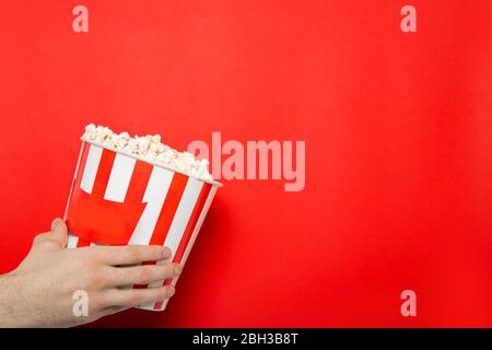 The guy holds popcorn in his hands on a red background. Place for text. Stock Photo