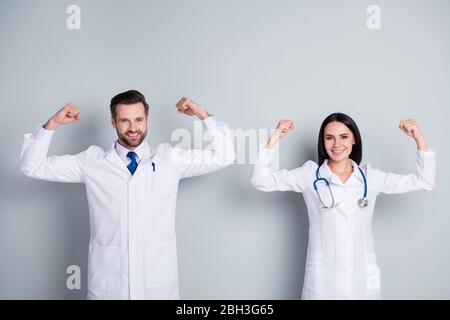 We save lives. Photo of doc practitioner guy experienced professional lady virology clinic specialists raise strong fists show biceps muscles wear lab Stock Photo