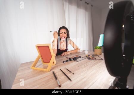 Young female vlogger doing makeup tutorial video for web channel at home - Happy influencer girl having fun filming with mobile smartphone Stock Photo