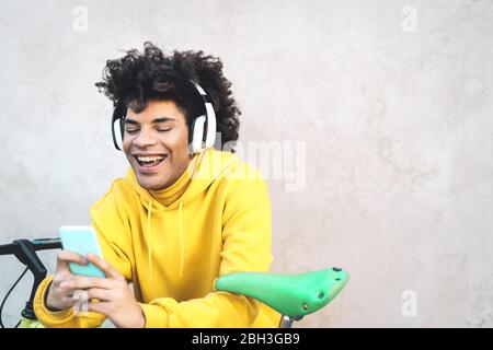 Happy Afro man using mobile smartphone outdoor - Young guy having fun listening music with wireless headphones Stock Photo